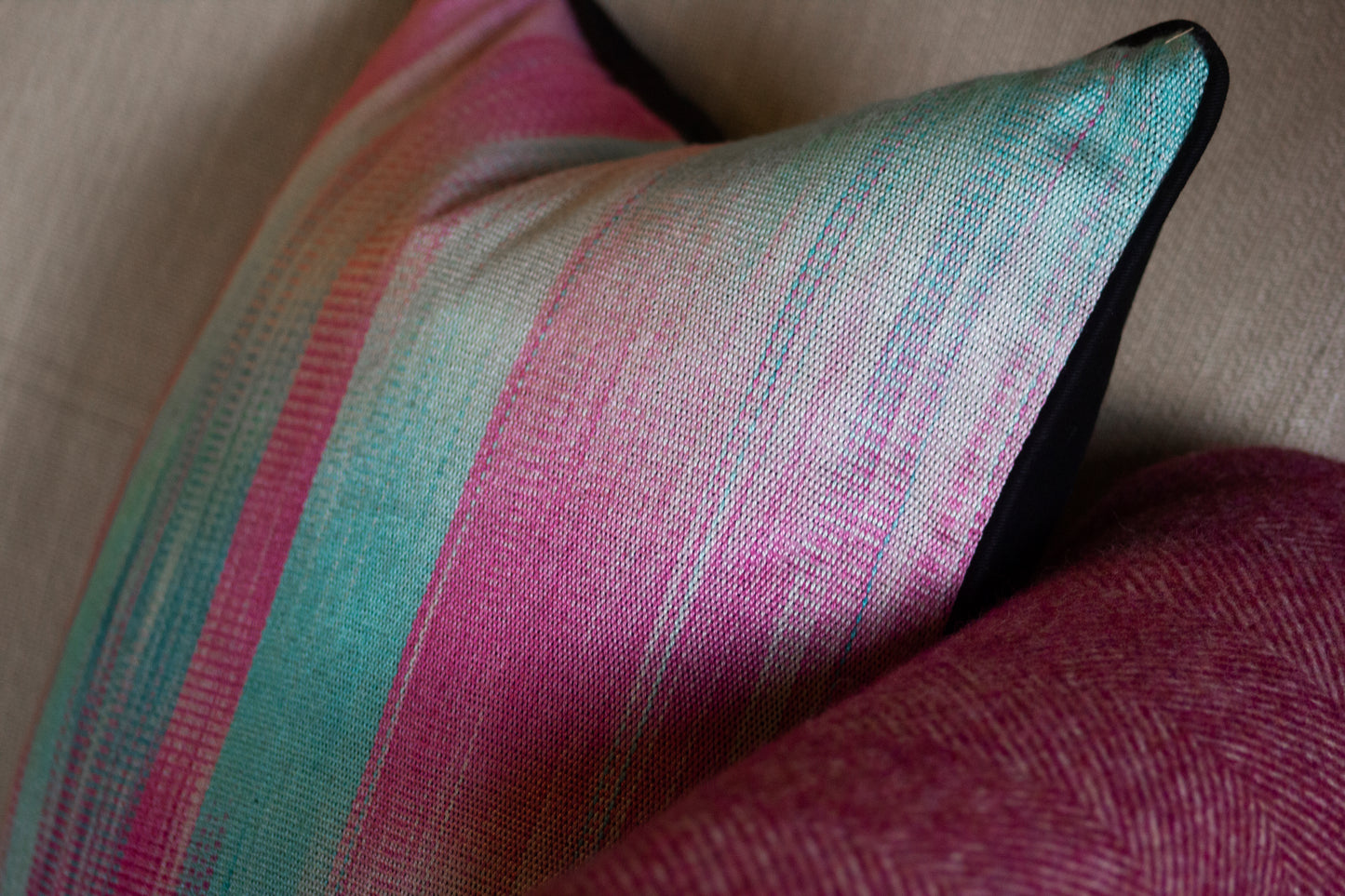 Close-up of a silk cushion with pink and aqua stripes, black edging, and a textured woven surface.