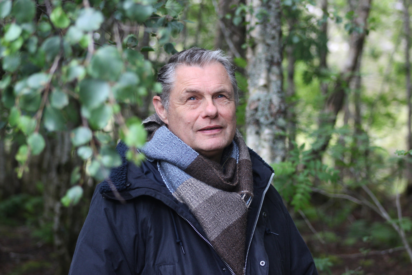 Horizontal striped alpaca handwoven blue, beige and brown scarf. Worn by male model in silver birch wood.